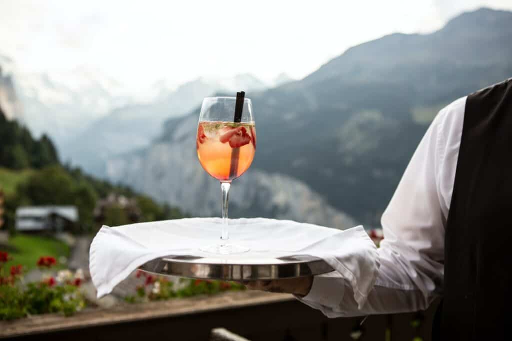 waiter holding tray with drink with mountains in the background