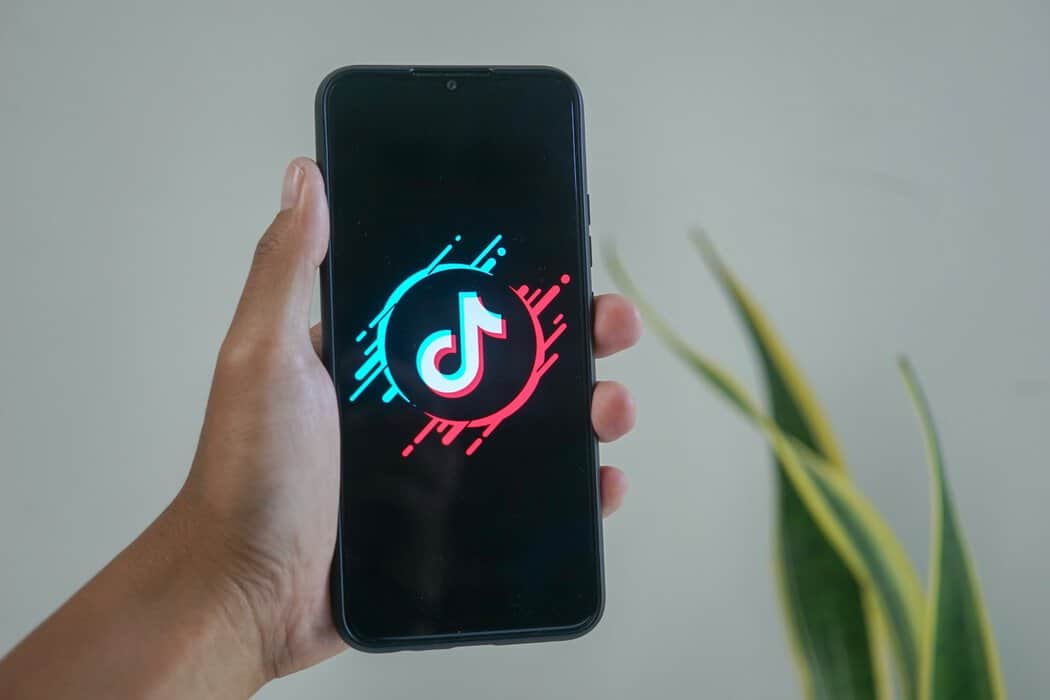 a person holding a cell phone with a neon logo on it - short form video tiktok logo