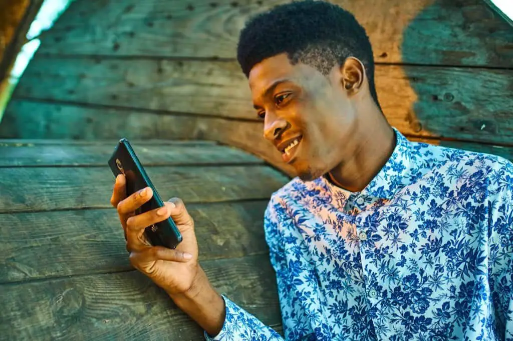 man in blue and white floral button up shirt holding black smartphone