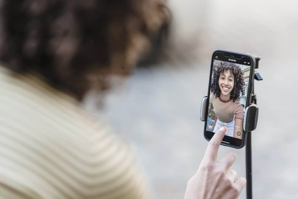 Crop cheerful young ethnic female vlogger touching screen on cellphone while preparing for video record in townbirthday campaign