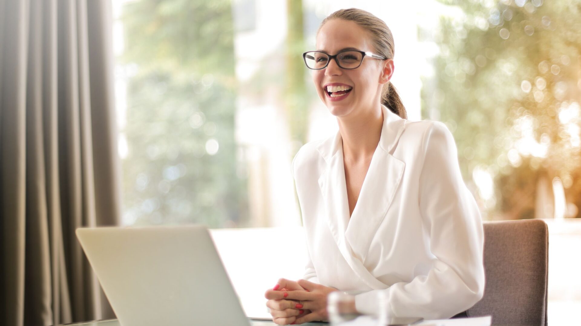 A young woman is seen happily recording a voice message on her smartphone, standing by a window holding a green cup at home. She is dressed casually, with her attention focused on the device, capturing a moment of modern communication. Zoho marketing automation