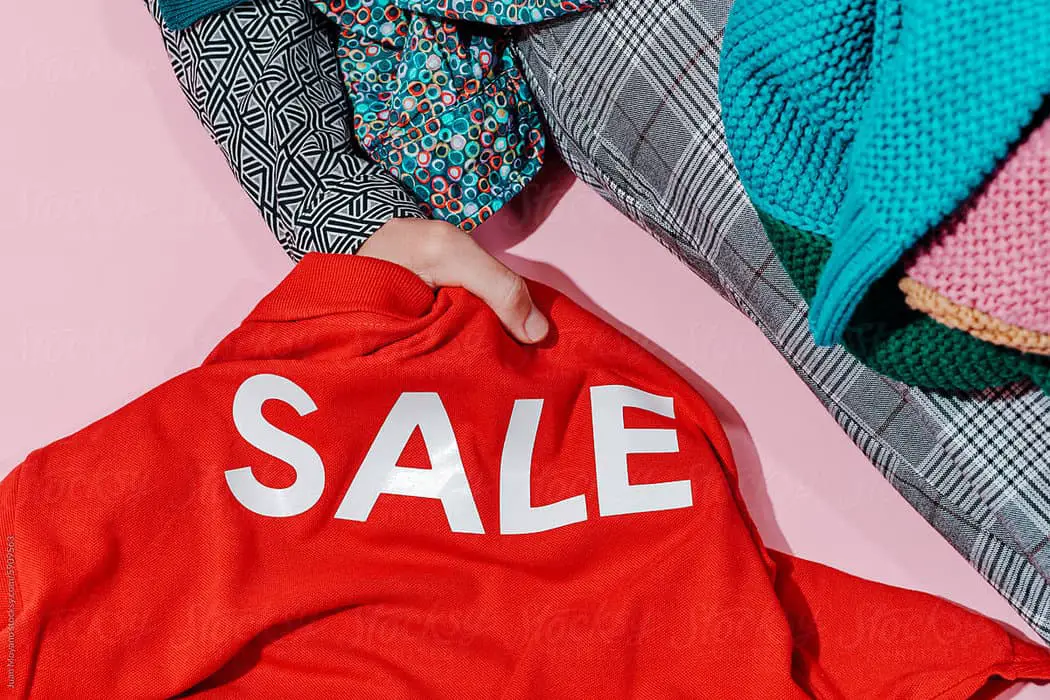 gmail ads- closeup of a man lying on a pink surface covered by different clothes while is grabbing a red shirt with the word sale printed on it