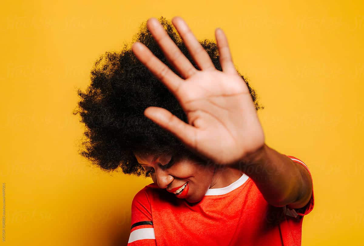 hide my email - From above of young woman with curly hair showing stop gesture and looking down against yellow background